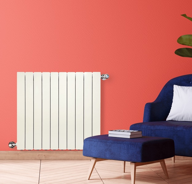 Cream aluminum radiator against a coral wall beside a navy armchair